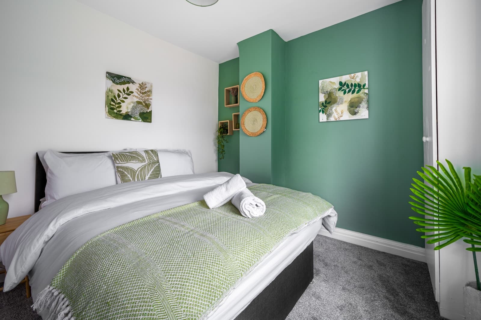 A made-up double bed with fresh linen, folded towels and a green feature wall